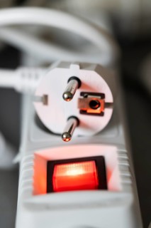 Close-up of a white power plug, Schuko plug, on a multiple socket with red indicator light,