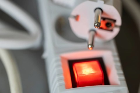 Close-up of a white power plug, Schuko plug, on a multiple socket with red indicator light,