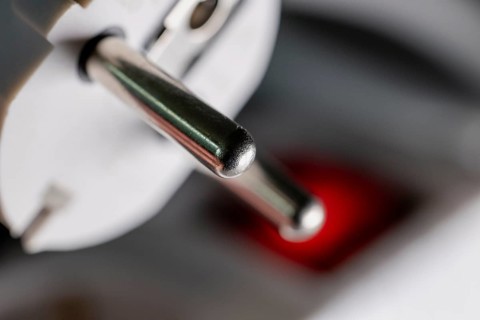 Close-up of a white power plug, Schuko plug, on a multiple socket with red indicator light,