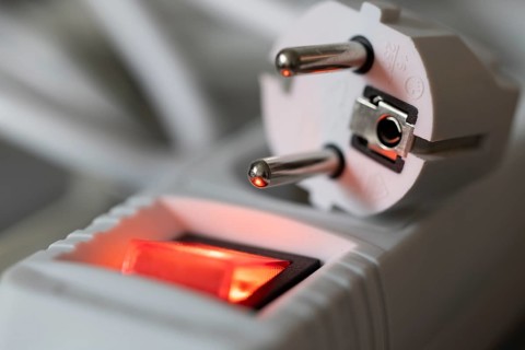 Close-up of a white power plug, Schuko plug, on a multiple socket with red indicator light,