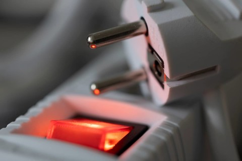 Close-up of a white power plug, Schuko plug, on a multiple socket with red indicator light,