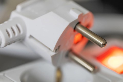 Close-up of a white power plug, Schuko plug, on a multiple socket with red indicator light,
