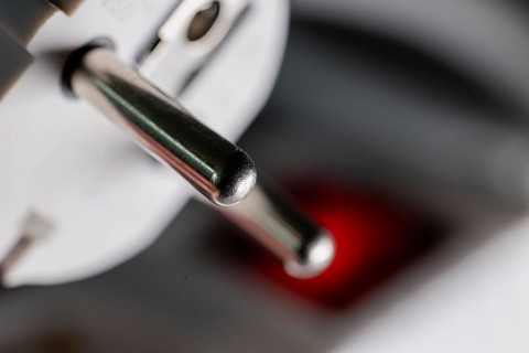Close-up of a white power plug, Schuko plug, on a multiple socket with red indicator light,