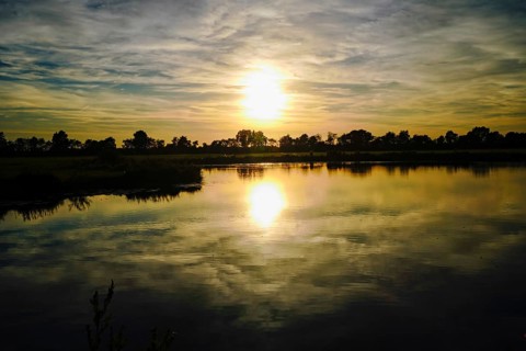 The setting sun paints the sky in warm colours that are reflected in the lake, natural landscape in
