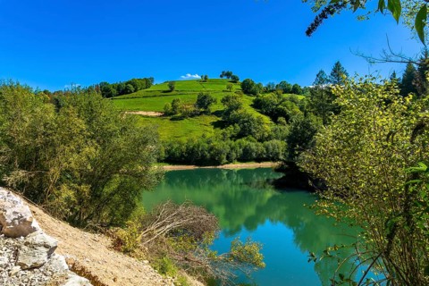Ibiur reservoir reflects the surrounding green hills and lush vegetation under a clear blue sky,