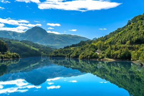 The serene ibiur reservoir in tolosa, gipuzkoa, reflects the surrounding mountains and blue sky
