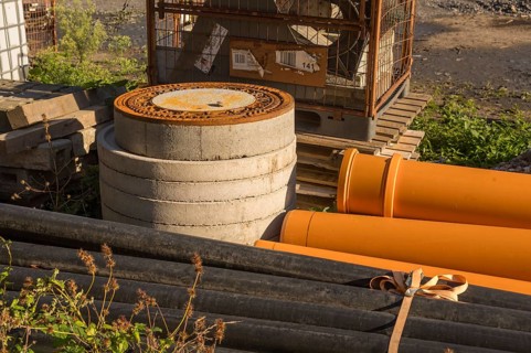 Borken, NRW, Germany, Orange and black pipes, concrete rings, and a rusty manhole cover sit at a