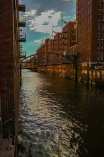 Sunlight is reflected in the water of the canal between tall brick buildings. View from the