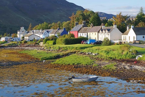 A quiet seaside village with colourful houses, a boat in the water and a green landscape against a