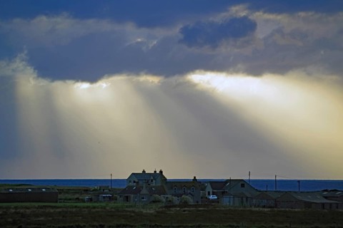 Sunbeams break through dramatic clouds over houses by the sea, John O Groats, Scotland, Great
