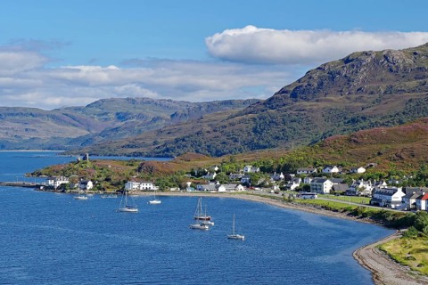 Coastal town with sailing boats at the harbour, mountains in the background, under blue sky, Kyle