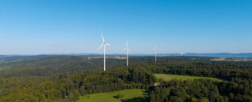 Wind turbines stand above a wooded hill under a clear blue sky, near Schorndorf, Rems Valley,