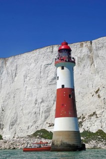Red lighthouse and boat near white cliffs by the sea, Beachy Head Lighthouse, Bournemouth, Dorset,
