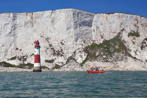 Red lighthouse and boat near white cliffs by the sea, Beachy Head Lighthouse, Bournemouth, Dorset,
