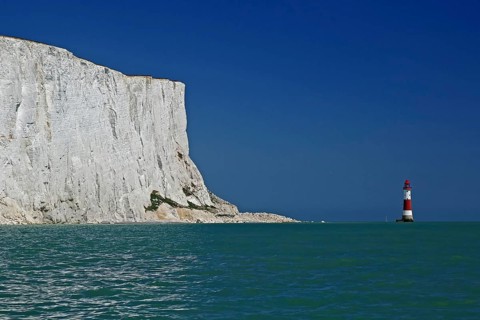 White cliff top next to a red and white lighthouse under a clear blue sky by the sea, Old Harrys