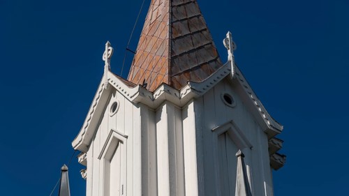 Pointed church tower with wooden elements and clear blue sky in the background, Tangen kirke or