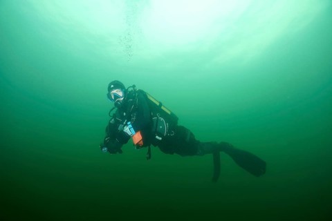 Diver underwater in greenish water with diving equipment during a safety stop. Dive site wreck of