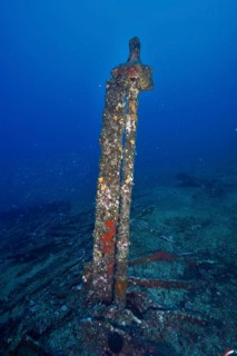 Old rusty part of a shipwreck standing on the seabed, surrounded by blue waters. Dive site wreck Le