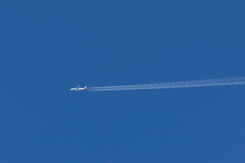 Jet passenger aircraft of Austrian Airways flying with vapour trails or contrails behind in a blue