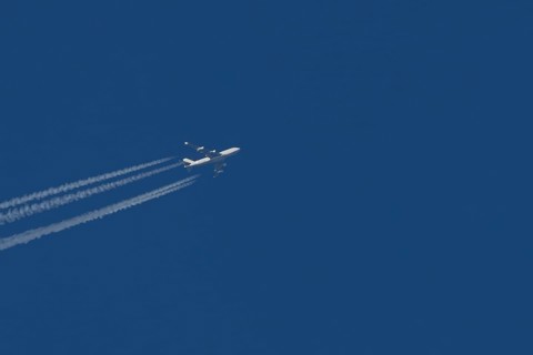Boeing 747 Jumbo jet cargo aircraft in flight in a blue sky with vapour trails or contrails behind,
