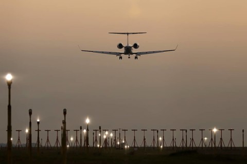 Executive business jet passenger aircraft landing over runway lights at sunset, London Stansted