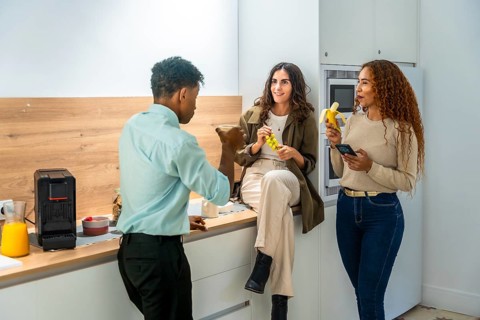Diverse colleagues chatting and smiling during a casual office kitchen break, two women holding