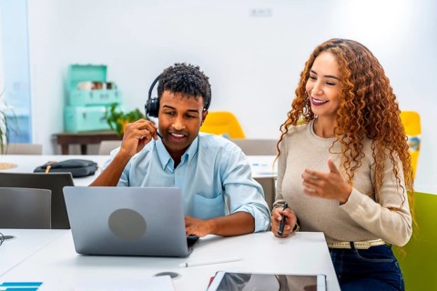 Diverse colleagues at an office desk collaborate as a man with a headset uses a laptop while a