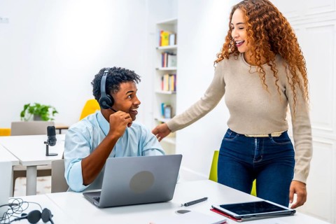Multiracial coworkers smiling and interacting in a modern office, with a man wearing a headset