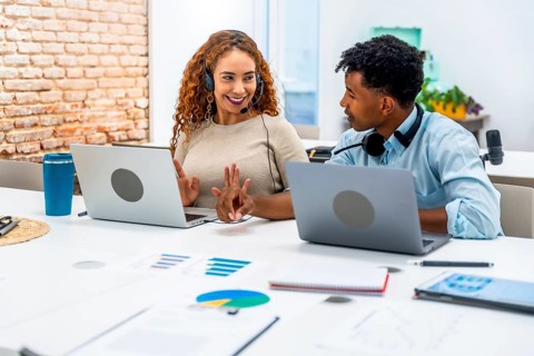 Diverse male and female coworkers with headsets collaborate at laptops on a bright modern office
