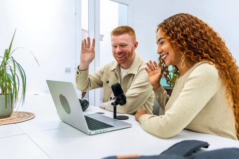 Diverse young adult man and woman smiling and waving while actively recording a podcast or