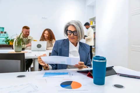 Mature female manager reviewing a financial report with charts and graphs on a table, collaborating