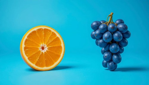 A halved orange and a bunch of dark blue grapes are set against a bright, solid blue backdrop,