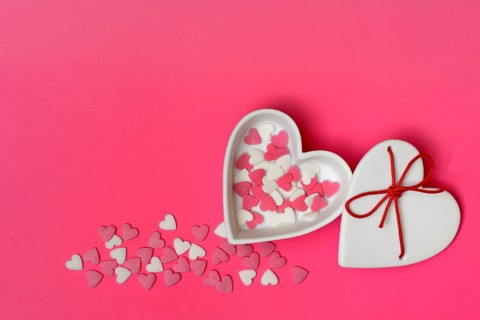 Sugar hearts in a heart-shaped bowl on a pink background