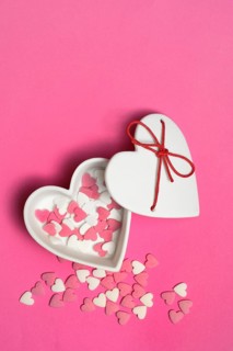 Sugar hearts in a heart-shaped bowl on a pink background