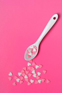 Sugar hearts with spoon on pink background