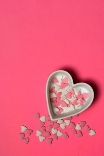 Sugar hearts in a heart-shaped bowl on a pink background