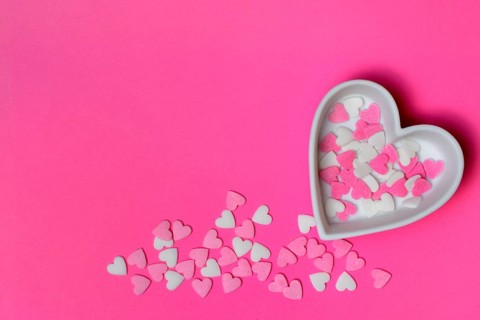 Sugar hearts in a heart-shaped bowl on a pink background