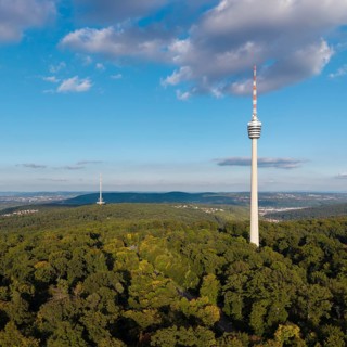 View of the television tower above a green forest under a blue sky with soft clouds,