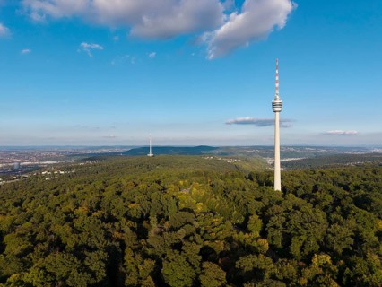 The television tower above a wooded area shows a clear sky and scattered clouds,