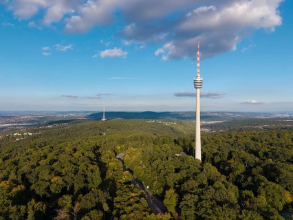 Television tower rises out of lush forest, surrounded by blue sky and decorated with clouds,