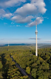 View of a television tower above a dense forest, surrounded by soft clouds in the sky,