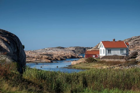 White houses and falun red boathouse on grassy shore, Bohus granite, rocky coast, Ramsvik,