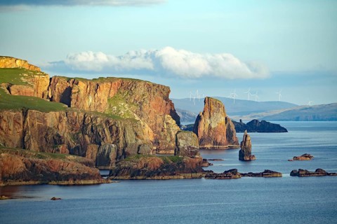 Cliffs and rock formations by the sea with wind turbines in the background, Eshaness, Shetland