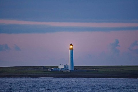 Lighthouse at dusk illuminating the sea, Orkney Islands, Scotland, Great Britain