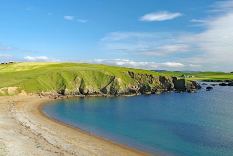 Sandy beach beach and blue sea with green cliffs under a clear sky, Eshaness, Shetland Islands,