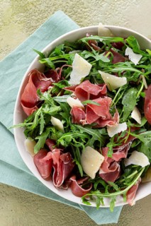 Fresh arugula salad with prosciutto and grated parmesan cheese, on a plate, homemade, no people
