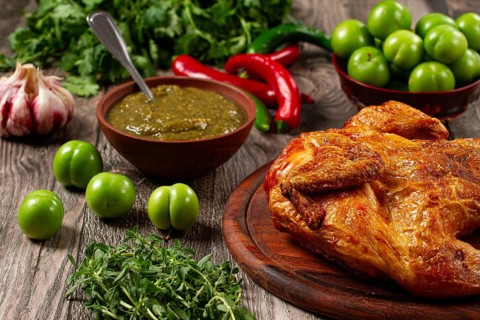 Baked tobacco chicken, served with tkemali sauce, on a wooden table, Georgian cuisine, rustic