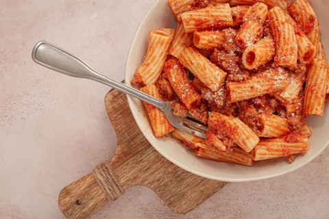 Rigatoni pasta with meat sauce and parmesan cheese on a light table, top view, homemade, no people