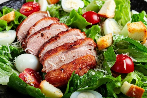 Caesar salad, with duck breast, on a black plate, on a light background, homemade, no people