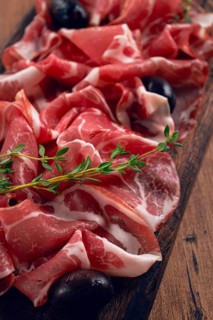 Freshly cut dried meat, served with olives and herbs, on a wooden chopping board, no people